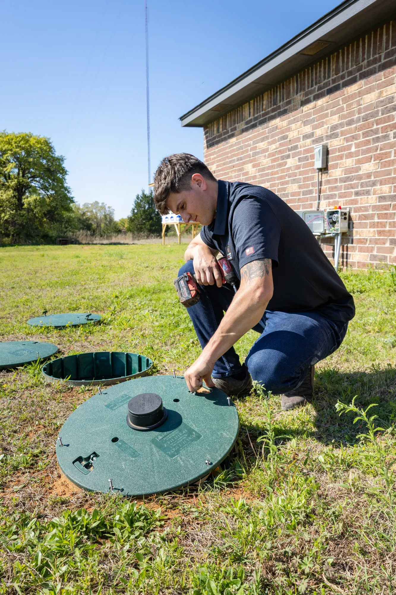 K&M technician opening a septic tank riser lid beside a brick home